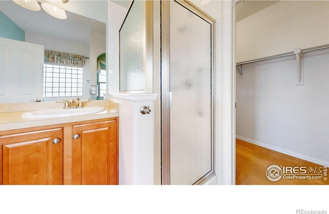 full bathroom with a stall shower, a spacious closet, and vanity