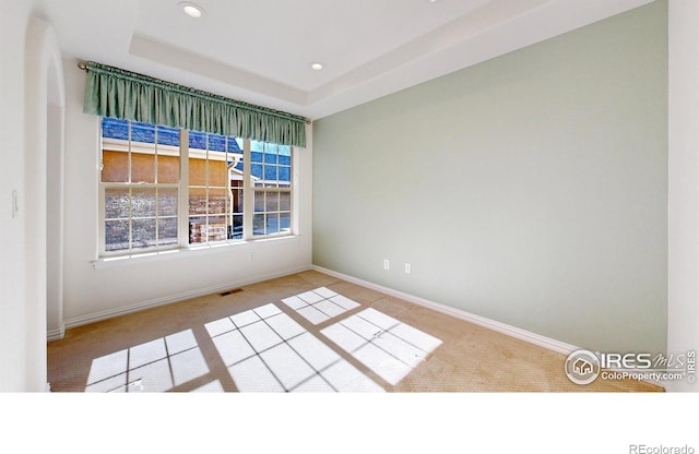 carpeted empty room featuring baseboards, visible vents, a raised ceiling, and recessed lighting