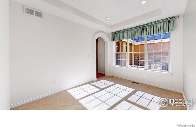 carpeted empty room with arched walkways, a raised ceiling, visible vents, and recessed lighting