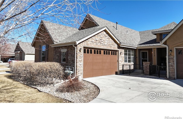 view of front of property featuring a garage, stone siding, a shingled roof, and concrete driveway