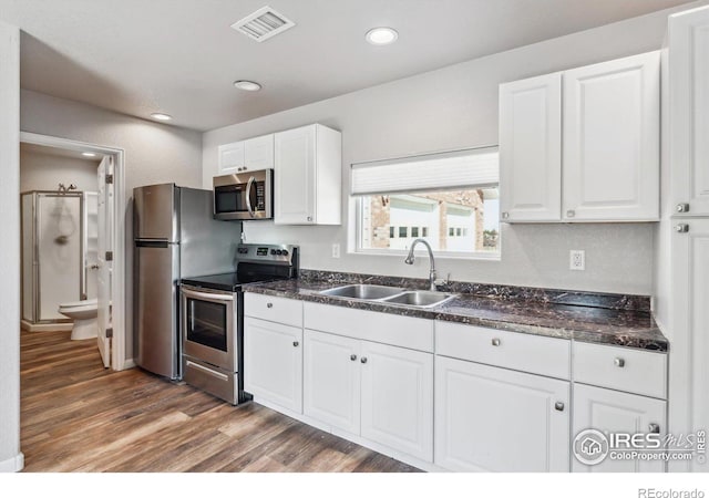 kitchen with dark countertops, wood finished floors, white cabinets, stainless steel appliances, and a sink