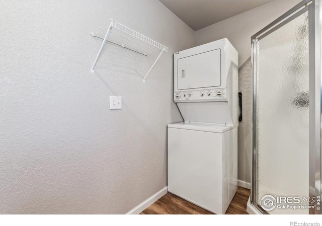 clothes washing area with laundry area, baseboards, stacked washer / drying machine, and dark wood-type flooring