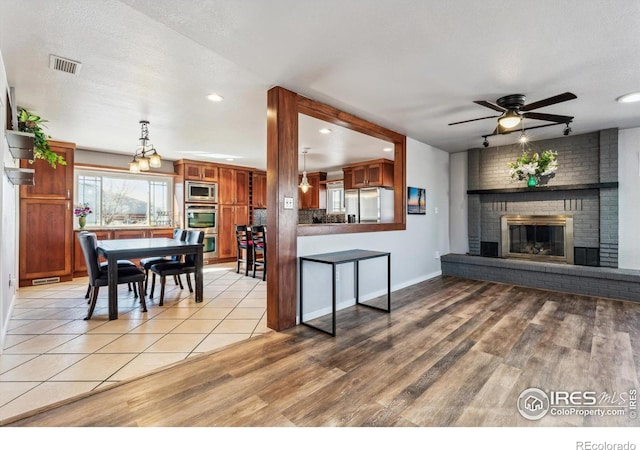 interior space with a brick fireplace, a ceiling fan, visible vents, and light wood-type flooring