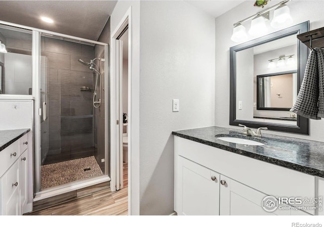 bathroom with a shower stall, vanity, toilet, and wood finished floors