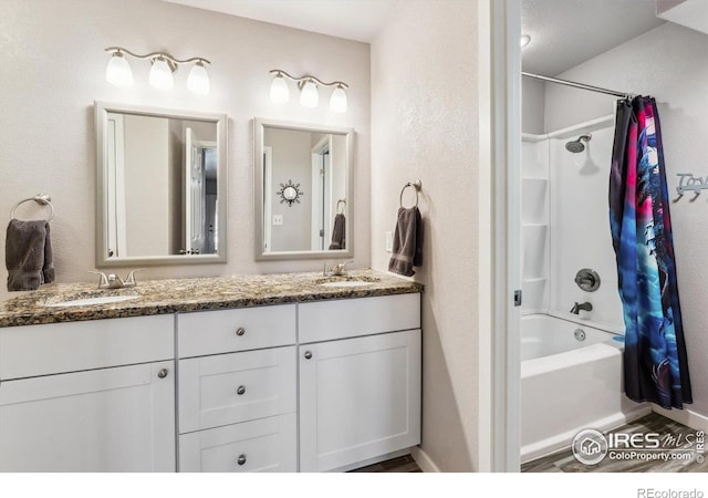 full bath featuring double vanity, wood finished floors, shower / bath combo with shower curtain, and a sink