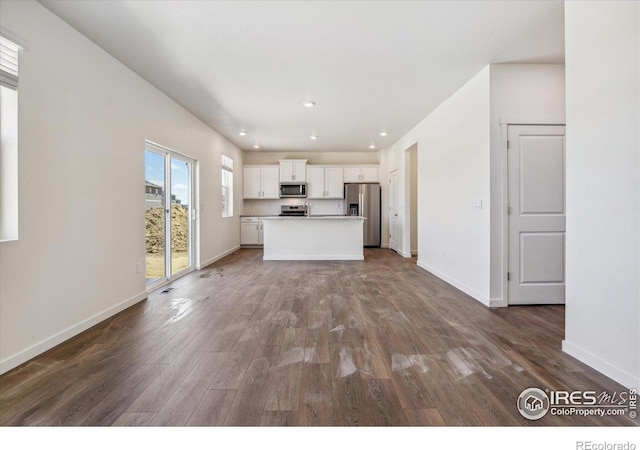 kitchen featuring baseboards, dark wood-style floors, appliances with stainless steel finishes, a center island, and white cabinetry