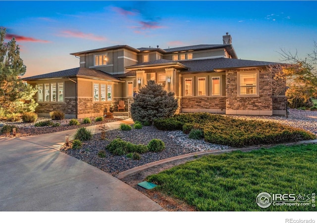 prairie-style home featuring stone siding, a chimney, and stucco siding