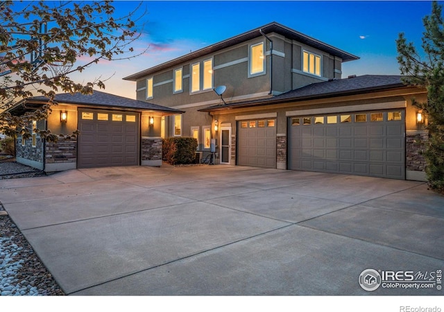 prairie-style home featuring an attached garage, stone siding, concrete driveway, and stucco siding