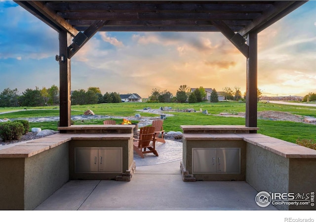 patio terrace at dusk featuring a lawn, area for grilling, and a pergola