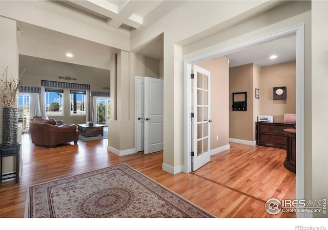 corridor with light wood finished floors, baseboards, coffered ceiling, and beam ceiling