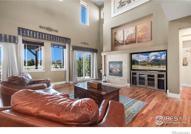 living area with a high ceiling, a fireplace, baseboards, and wood finished floors