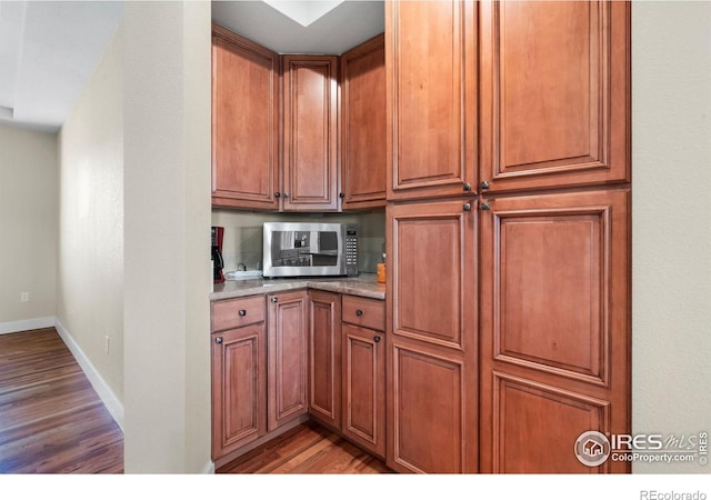 kitchen featuring stainless steel microwave, brown cabinets, light wood-style flooring, and baseboards