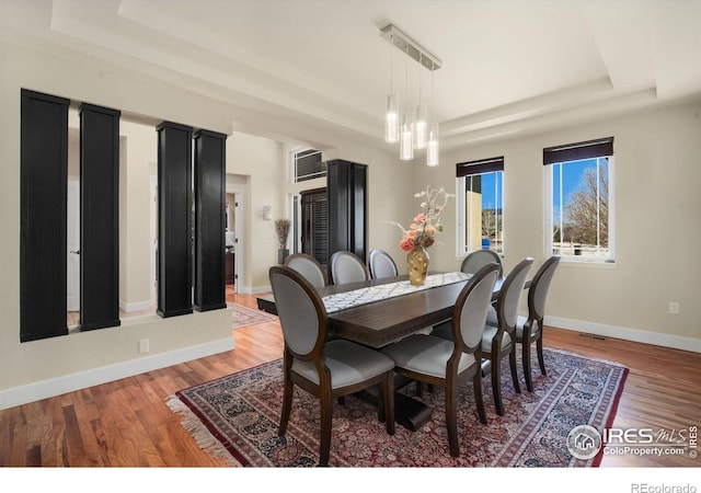 dining space featuring light wood-style flooring, a tray ceiling, a chandelier, and baseboards