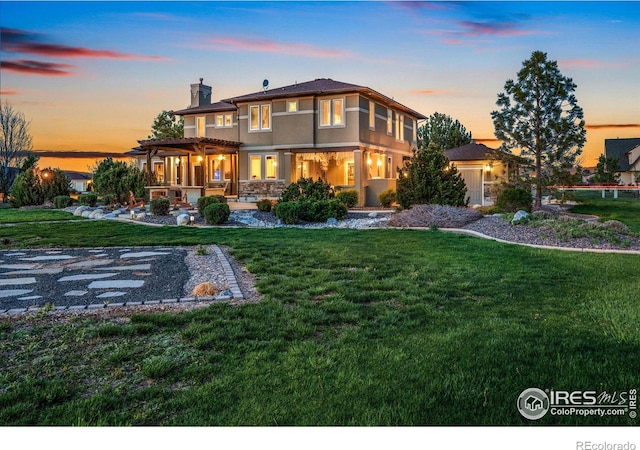 back of property at dusk featuring stucco siding, a chimney, a pergola, and a yard