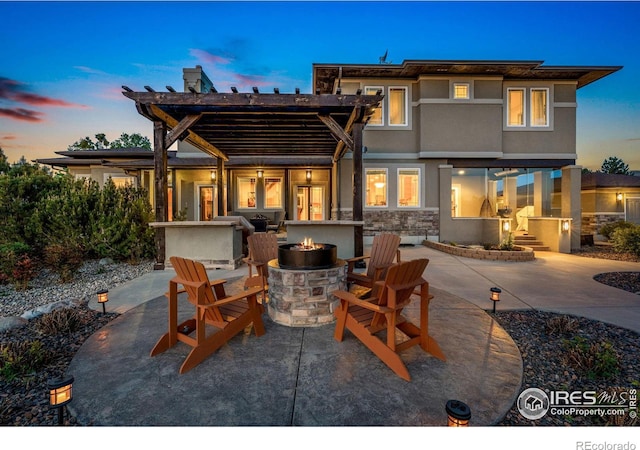 back of house at dusk featuring a fire pit, a patio, and stucco siding