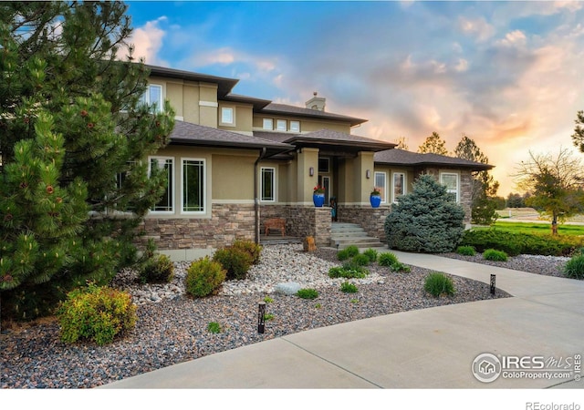 prairie-style house featuring stone siding, a chimney, and stucco siding