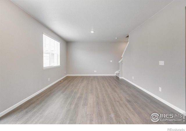 spare room featuring stairs, wood finished floors, and baseboards