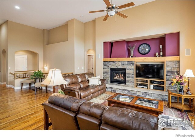 living area featuring wood finished floors, baseboards, a fireplace, arched walkways, and a towering ceiling