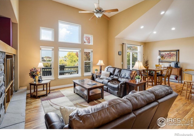 living room with light wood finished floors, a stone fireplace, baseboards, and a towering ceiling