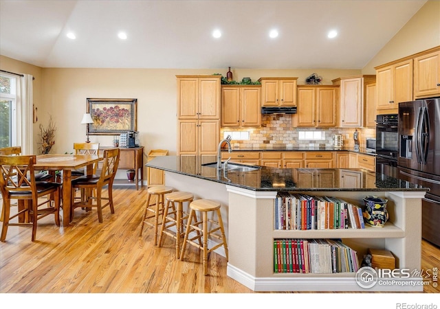 kitchen featuring a breakfast bar area, lofted ceiling, a sink, black appliances, and under cabinet range hood