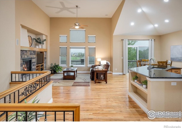 13943 W 87th Ln, Arvada, CO 80005 - living area with light wood-type flooring, a ceiling fan, a stone fireplace, recessed lighting, and a high ceiling