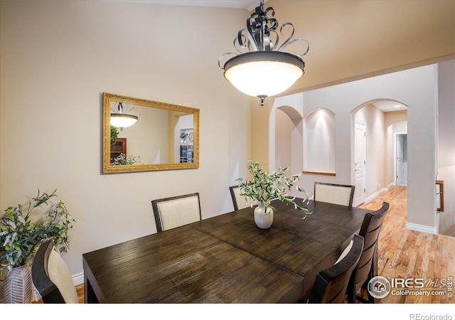 13943 W 87th Ln, Arvada, CO 80005 - dining space featuring arched walkways, light wood finished floors, a chandelier, and baseboards