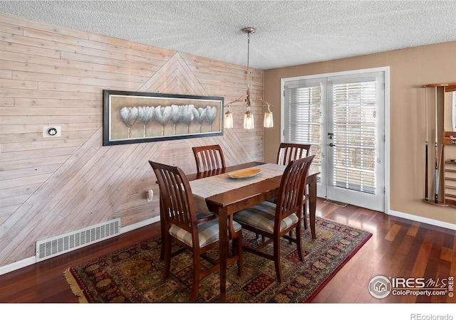 dining room featuring a textured ceiling, wood walls, wood finished floors, visible vents, and baseboards