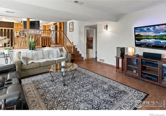 living room featuring tile patterned flooring, stairs, visible vents, and a textured ceiling