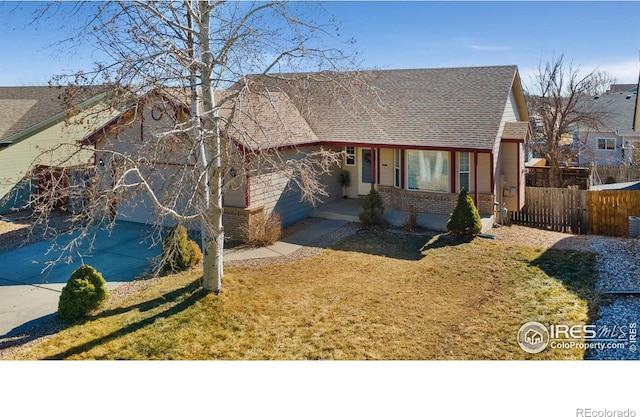 view of front of home with brick siding, fence, a front lawn, and roof with shingles