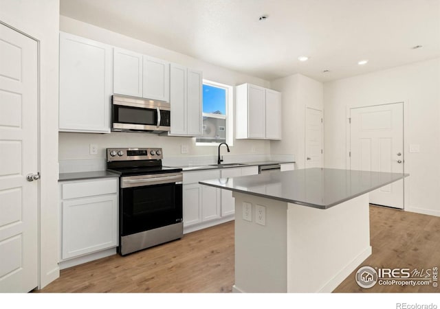 kitchen featuring a kitchen island, stainless steel appliances, light wood-style floors, white cabinetry, and a sink