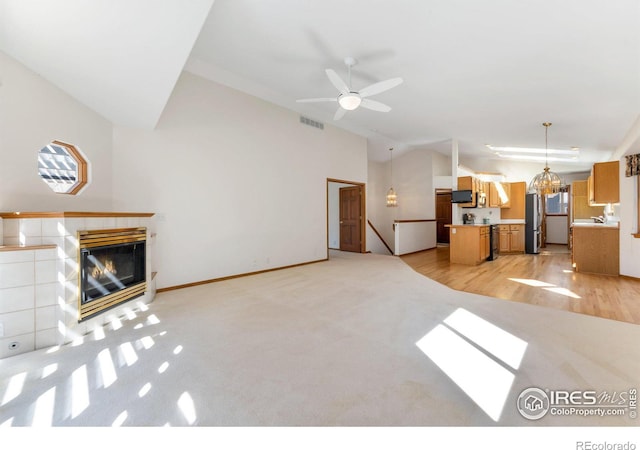 unfurnished living room with lofted ceiling, visible vents, a tiled fireplace, baseboards, and ceiling fan with notable chandelier