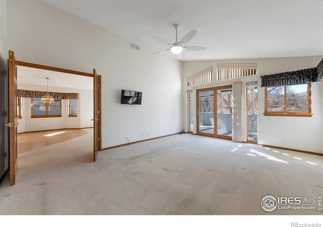 carpeted empty room with high vaulted ceiling, baseboards, visible vents, and ceiling fan with notable chandelier