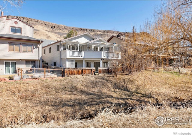 rear view of property featuring fence, a balcony, and a mountain view