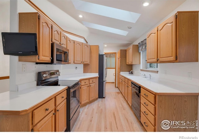 kitchen with vaulted ceiling with skylight, recessed lighting, stainless steel appliances, a sink, and light wood-type flooring