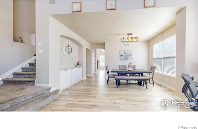 dining area with arched walkways, a wealth of natural light, and light wood-style floors