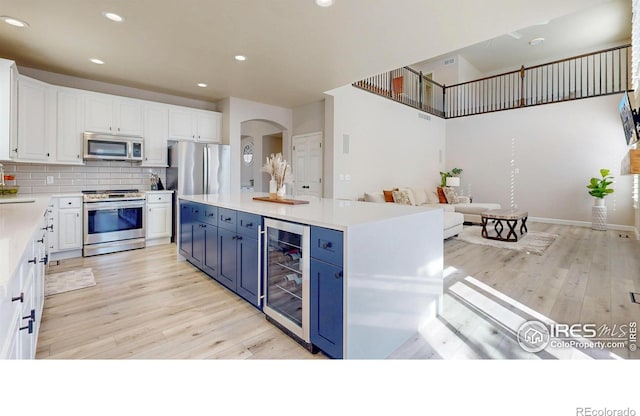 kitchen with wine cooler, backsplash, appliances with stainless steel finishes, white cabinets, and blue cabinets