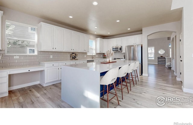 kitchen featuring arched walkways, a breakfast bar area, tasteful backsplash, appliances with stainless steel finishes, and white cabinets