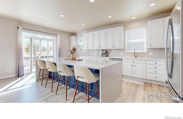 kitchen with white cabinets, decorative backsplash, light wood-style flooring, a kitchen island, and freestanding refrigerator