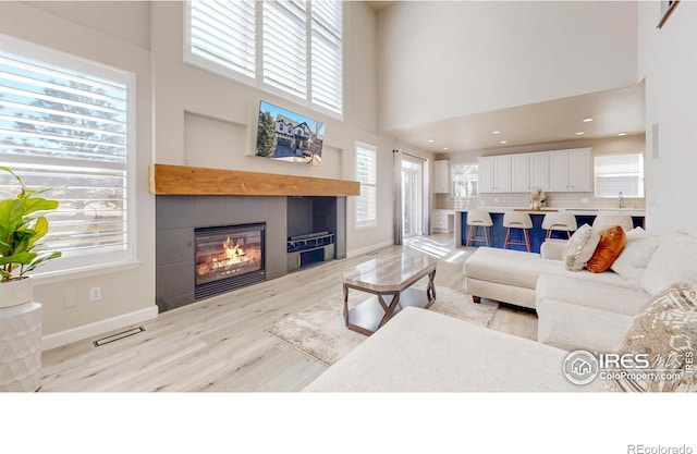 living area featuring light wood-style floors, a high ceiling, baseboards, and a tiled fireplace