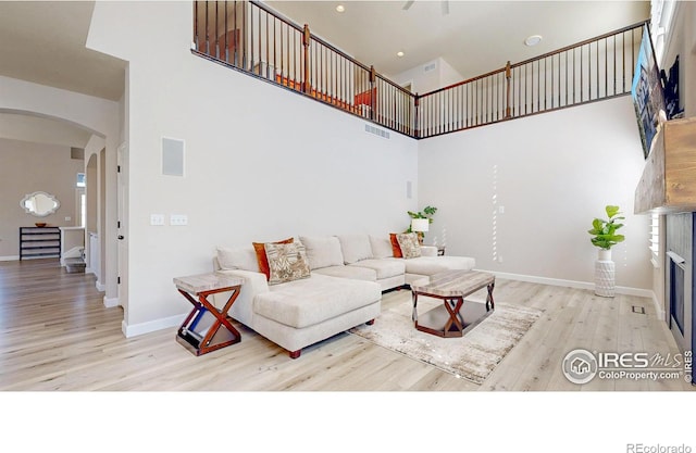 living room featuring arched walkways, wood finished floors, visible vents, a towering ceiling, and baseboards