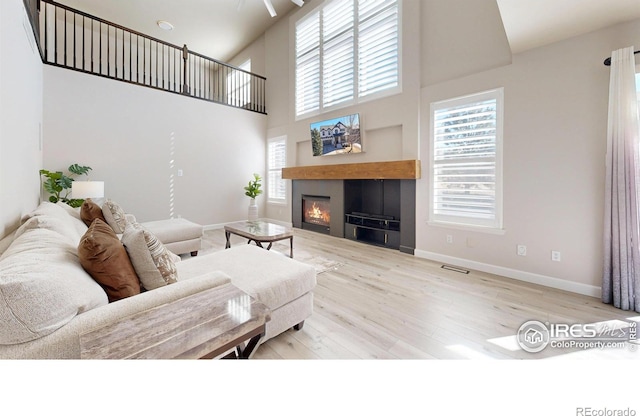 living area with a glass covered fireplace, wood finished floors, a towering ceiling, and baseboards