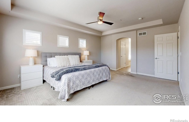 carpeted bedroom with arched walkways, a raised ceiling, visible vents, and baseboards