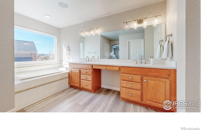 bathroom with double vanity, wood finished floors, a sink, and a bath