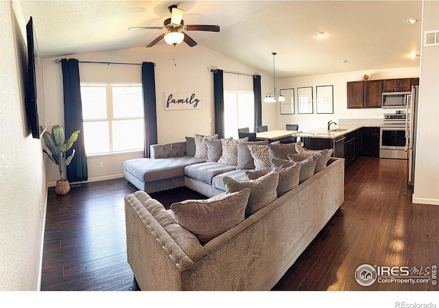 living area with visible vents, dark wood-type flooring, vaulted ceiling, baseboards, and ceiling fan with notable chandelier