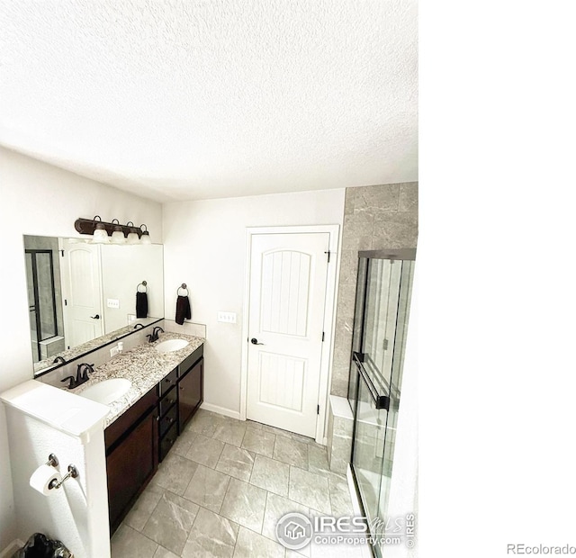 bathroom featuring double vanity, a textured ceiling, an enclosed shower, and a sink