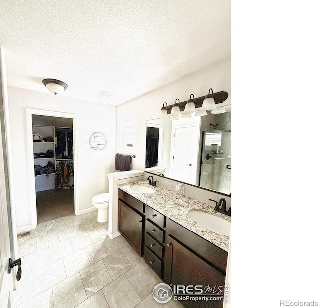 full bath featuring double vanity, a spacious closet, a textured ceiling, and a sink