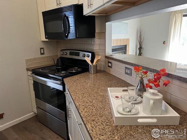 kitchen featuring black microwave, light stone counters, stainless steel electric stove, white cabinetry, and decorative backsplash