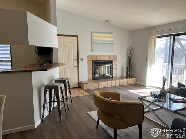 living area featuring lofted ceiling, a fireplace, baseboards, and wood finished floors