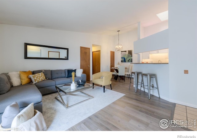 living room featuring light wood-style floors, baseboards, high vaulted ceiling, and an inviting chandelier