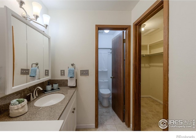 bathroom with tile patterned flooring, toilet, vanity, baseboards, and a spacious closet